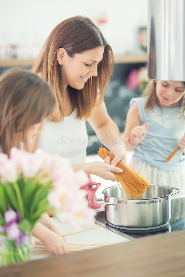 Mom με δύο νέες κόρες διδύμων στα μαγειρεύοντας μακαρόνια κουζινών στοκ φωτογραφίες Mom με δύο νέες κόρες διδύμων στα μαγειρεύοντας μακαρόνια κουζινών στοκ φωτογραφίες