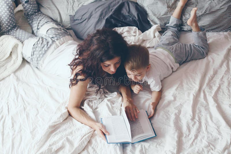 Young mother with her 2 years old little son dressed in pajamas are relaxing and playing in the bed at the weekend together, lazy morning, warm and cozy scene. Pastel colors, selective focus. Young mother with her 2 years old little son dressed in pajamas are relaxing and playing in the bed at the weekend together, lazy morning, warm and cozy scene. Pastel colors, selective focus.