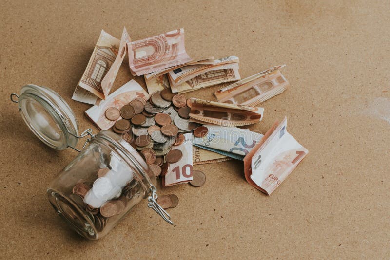 Cash money dropping from a glass jar on wooden table. Cash money dropping from a glass jar on wooden table.