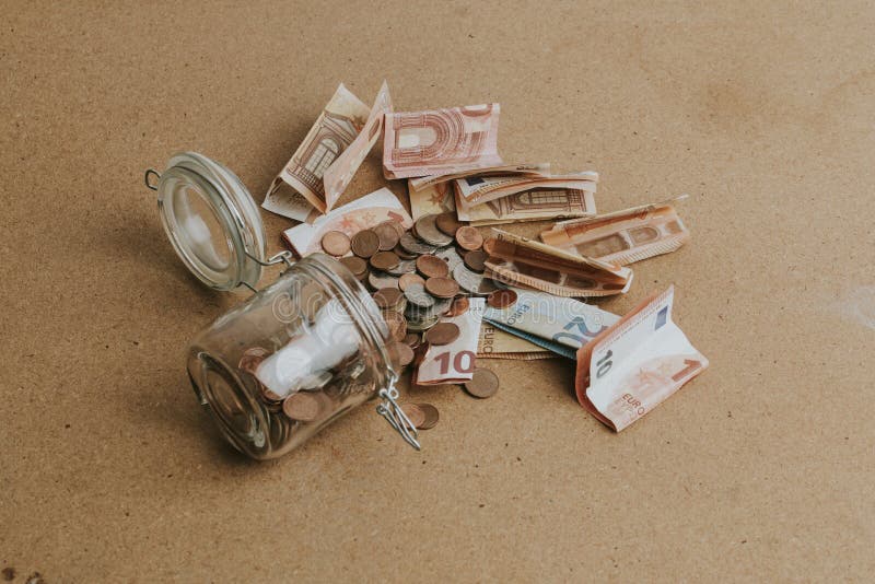 Cash money dropping from a glass jar on wooden table. Cash money dropping from a glass jar on wooden table.