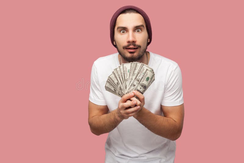 Money. Portrait of suprised handsome bearded young hipster man in white shirt and casual hat, stand, holding fan of dollars with stock photography Money. Portrait of suprised handsome bearded young hipster man in white shirt and casual hat, stand, holding fan of dollars with stock photography