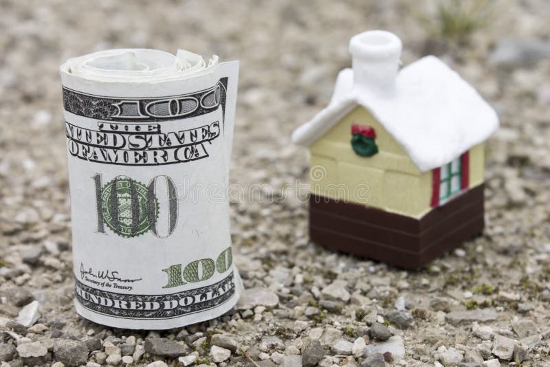 Money roll with small toy house on background. Real estate price concept. Selective focus royalty free stock photography Money roll with small toy house on background. Real estate price concept. Selective focus royalty free stock photography