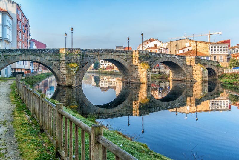 A beautiful wiew of old stone bridge Puente Vella or Puente Romano at sunrise and magic reflections in water of river Cabe. Monforte de Lemos, Galicia, Spain. Through this city passes the winter road of St. Jamesn. A beautiful wiew of old stone bridge Puente Vella or Puente Romano at sunrise and magic reflections in water of river Cabe. Monforte de Lemos, Galicia, Spain. Through this city passes the winter road of St. Jamesn