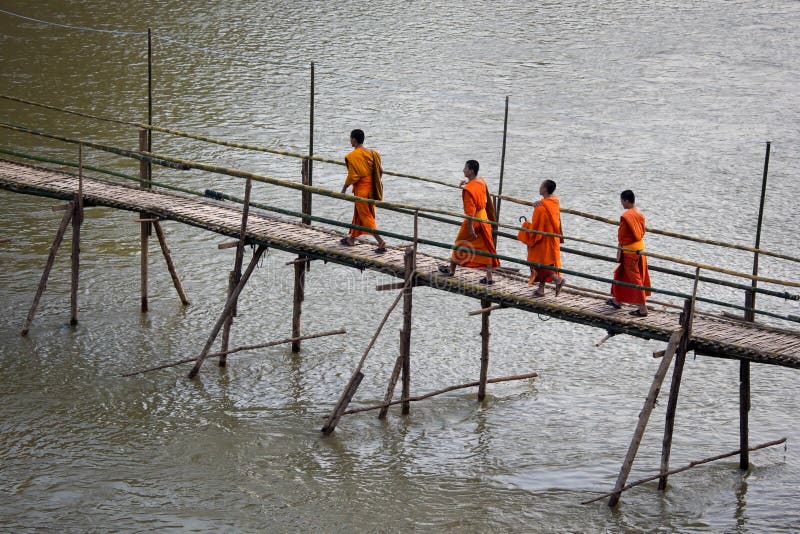 Monges budistas que cruzam a ponte de bambu em Luang Prabang, Laos imagem de stock Monges budistas que cruzam a ponte de bambu em Luang Prabang, Laos imagem de stock