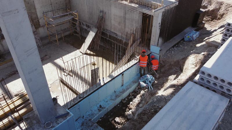 Monolitisk ramteknik inom byggindustrin. överblick över de anställda som är sysselsatta med byggnadsarbeten. byggare. Byggnadsarbetare isolerar grunden med skum. arbeta med förstärkta betongstrukturer.