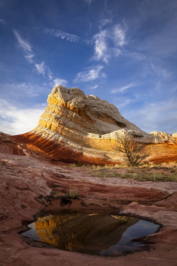 A yellow and red monolith rises up to meet the setting sun with a small pool reflecting in the foreground. A yellow and red monolith rises up to meet the setting sun with a small pool reflecting in the foreground.