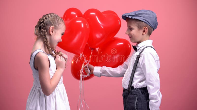 Monsieur mignon donnant à fille mignonne les ballons en forme de coeur, surprise de jour de valentines image libre de droits Monsieur mignon donnant à fille mignonne les ballons en forme de coeur, surprise de jour de valentines image libre de droits