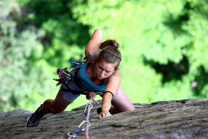 A concentrate female rock climber claiming a stone wall on a green forest background. A concentrate female rock climber claiming a stone wall on a green forest background