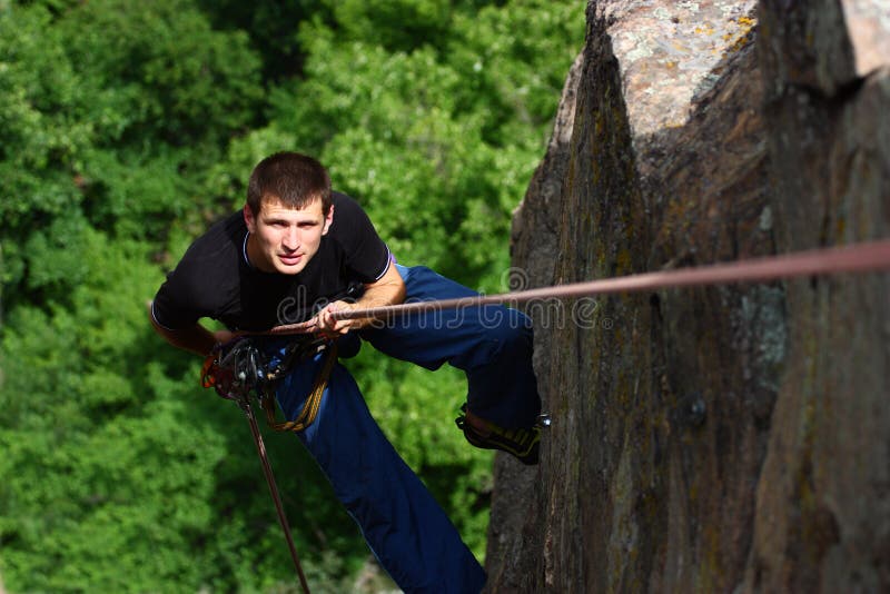 A male climber rappelling on a green forest background. A male climber rappelling on a green forest background