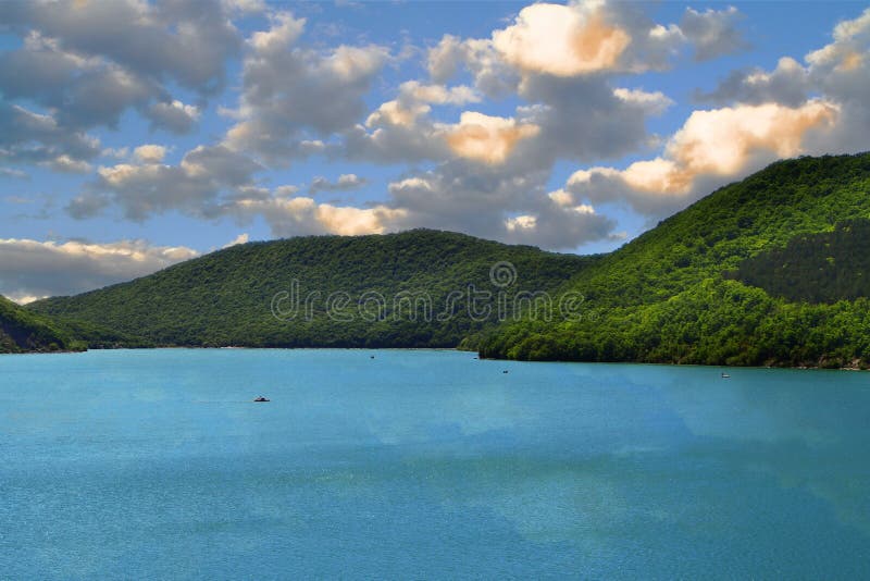 Montañas con el bosque verde en una orilla del lago en el cielo azul con el fondo de las nubes fotos de archivo Montañas con el bosque verde en una orilla del lago en el cielo azul con el fondo de las nubes fotos de archivo
