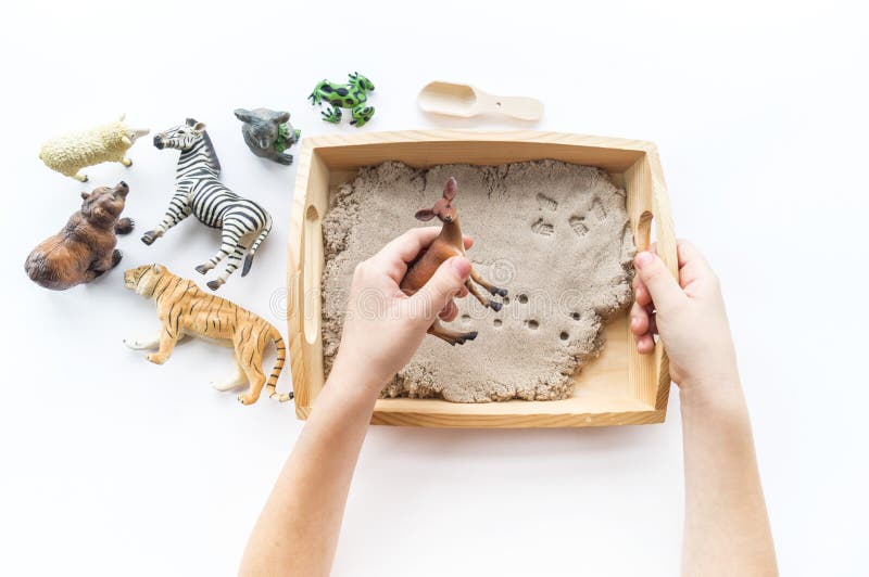 Montessori material. Children`s hands play an animal figure. Kinetic sand