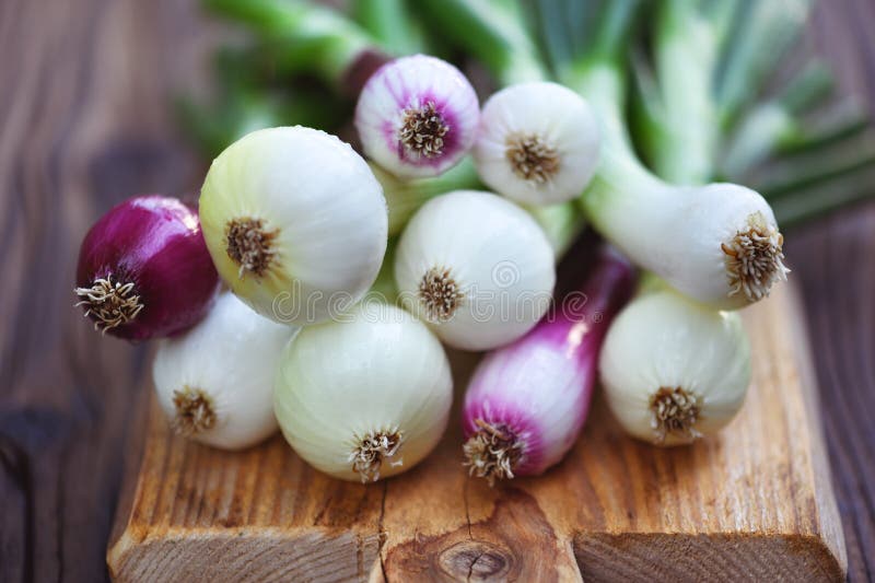Montón de cebollas frescas con verduras sobre una tabla de cortaduras de madera foto de archivo