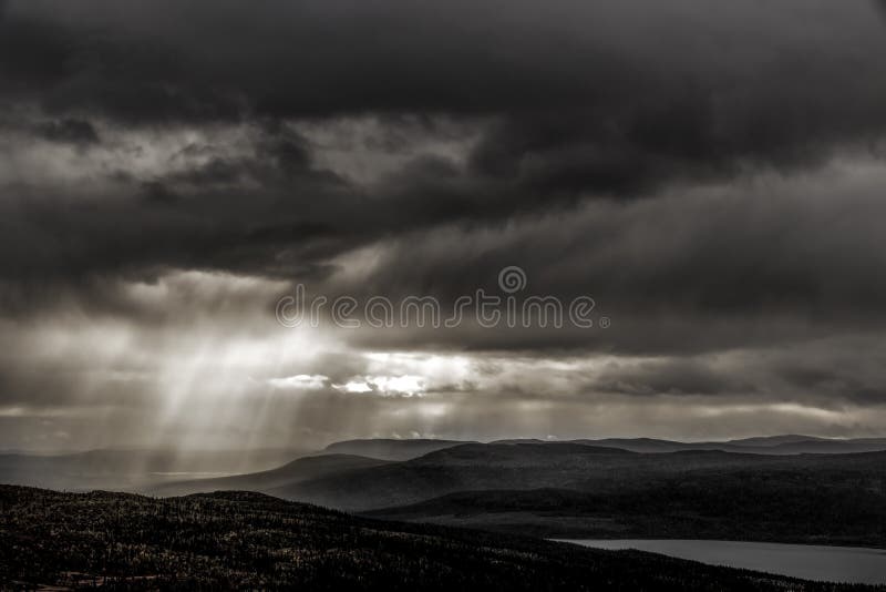 Moody woodland and lake landscape with sun beams through clouds