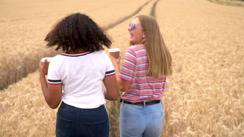Mooi blond meisje en tiener met gemengde rassen jonge vrouwen die een zonnebril dragen die koffie drinkt in een veld