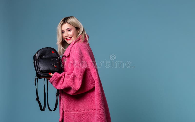 Mooi blondemeisje die roze laag dragen die zwarte rugzak in handen houden stock fotografie Mooi blondemeisje die roze laag dragen die zwarte rugzak in handen houden stock fotografie