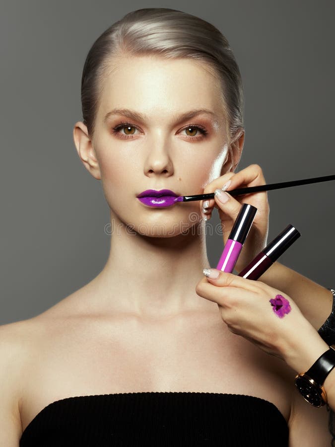 Mooi die meisje door handen van make-upkunstenaars met borstels en lippenstift dichtbij haar gezicht wordt omringd Foto van geluk stock fotografie Mooi die meisje door handen van make-upkunstenaars met borstels en lippenstift dichtbij haar gezicht wordt omringd Foto van geluk stock fotografie