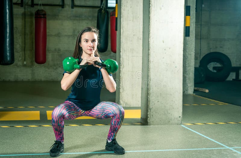 Mooi en knap jong meisje die twee ketelklokken in haar handen voor sterkte houden en geschiktheidstraining in de gymnastiek condi stock foto's Mooi en knap jong meisje die twee ketelklokken in haar handen voor sterkte houden en geschiktheidstraining in de gymnastiek condi stock foto's