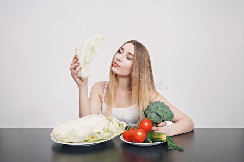 Mooi jong meisje bij een lijst met groenten voor salade Kok thuis Concept gezond, vegetarisch voedsel royalty-vrije stock foto Mooi jong meisje bij een lijst met groenten voor salade Kok thuis Concept gezond, vegetarisch voedsel royalty-vrije stock foto