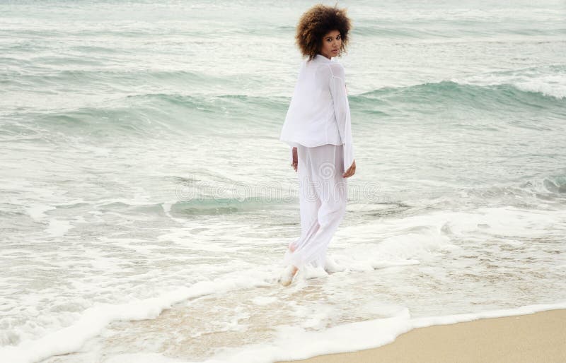 Mooi meisje met afrohaar en witte kledingsgang door het overzees royalty-vrije stock afbeelding Mooi meisje met afrohaar en witte kledingsgang door het overzees royalty-vrije stock afbeelding