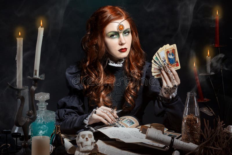 Mooi meisje met lange haarwijze in het beeld van de heks met de Tarotkaarten in zijn handen, zwarte lange valse spijkers met held stock afbeelding Mooi meisje met lange haarwijze in het beeld van de heks met de Tarotkaarten in zijn handen, zwarte lange valse spijkers met held stock afbeelding