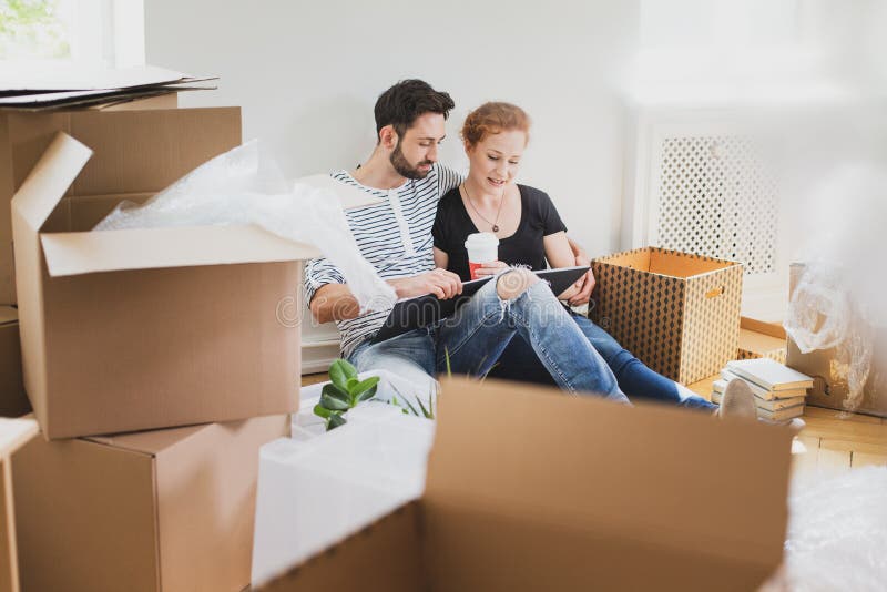 Mooi paar die fotoalbum bekijken terwijl het uitpakken van materiaal na verhuizing aan nieuw huis stock afbeeldingen Mooi paar die fotoalbum bekijken terwijl het uitpakken van materiaal na verhuizing aan nieuw huis stock afbeeldingen