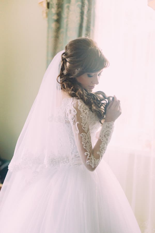Mooi portret van jonge vrouw in witte kleding en sluier bij ochtend dichtbij venster Krullend kapsel stock foto Mooi portret van jonge vrouw in witte kleding en sluier bij ochtend dichtbij venster Krullend kapsel stock foto