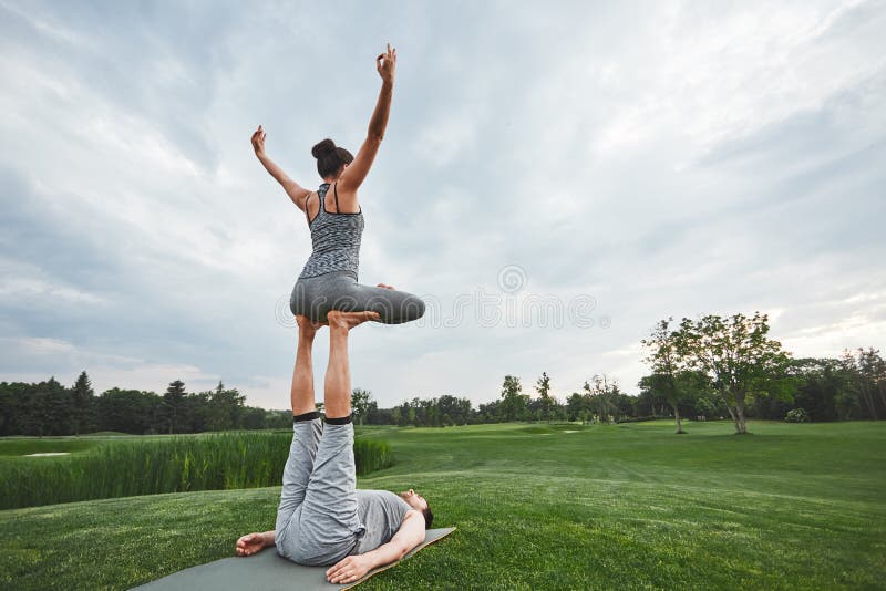 Mooi stelt met een partner De sterke man op een mat liggen en de in evenwicht brengende vrouw die in lotusbloem stellen op zijn v royalty-vrije stock fotografie Mooi stelt met een partner De sterke man op een mat liggen en de in evenwicht brengende vrouw die in lotusbloem stellen op zijn v royalty-vrije stock fotografie