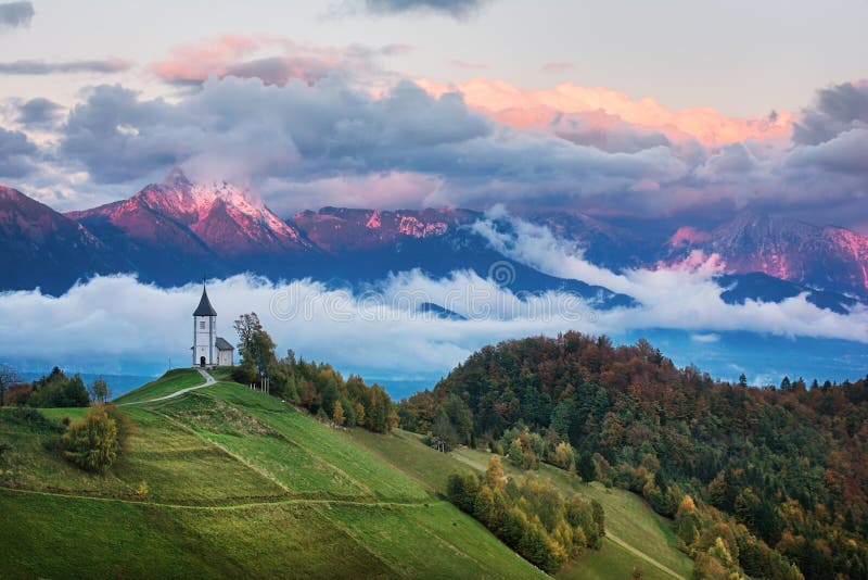 Mooi zonsopganglandschap van kerk Jamnik in Slovenië met bewolkte hemel