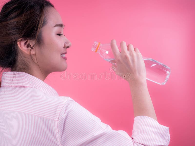 Mooie Aziatische jonge vrouw die die een fles water drinken op een roze achtergrond wordt geïsoleerd royalty-vrije stock afbeelding Mooie Aziatische jonge vrouw die die een fles water drinken op een roze achtergrond wordt geïsoleerd royalty-vrije stock afbeelding