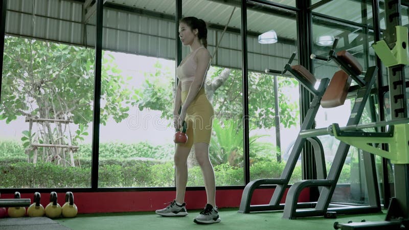 Mooie aziatische vrouw tilt een stalen bal op in de gym om haar spiermassa te versterken.