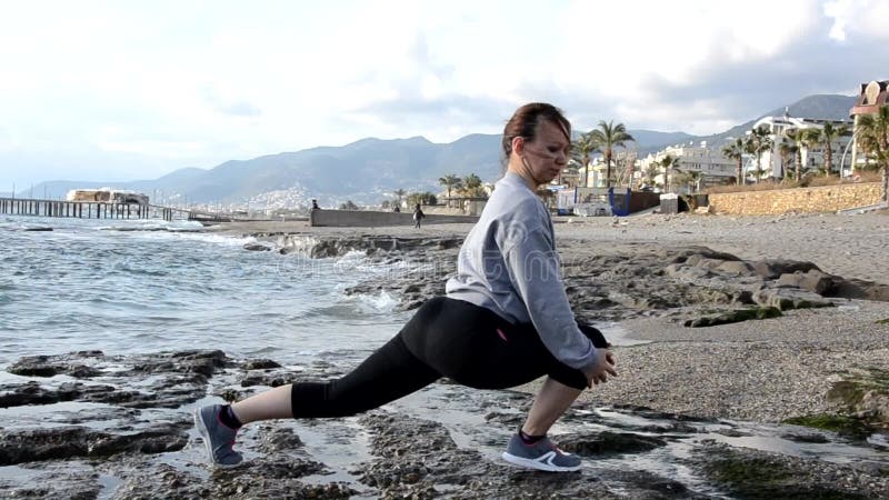 Mooie blond meisjeskleding in de zee aan de rots waar yoga zich uitstrekt tot sportgymnastiek en