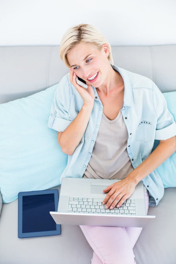 Mooie blondevrouw die haar laptop met behulp van terwijl het uitnodigen van de telefoon royalty-vrije stock foto's Mooie blondevrouw die haar laptop met behulp van terwijl het uitnodigen van de telefoon royalty-vrije stock foto's
