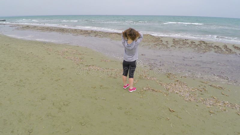 Mooie dame die met krullend haar verbazend mening over overzees genieten van, die zich op het strand bevinden