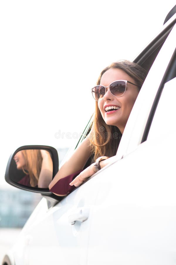 Portrait of young happy businesswoman sitting in her car and smiling. Lady with long brown hair in sunglasses looking away. Portrait of young happy businesswoman sitting in her car and smiling. Lady with long brown hair in sunglasses looking away.