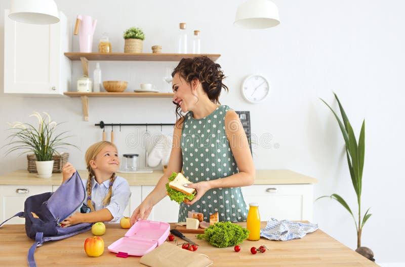 Mooie donkerbruine moeder en haar dochter die gezonde lunch inpakken en schooltas voorbereiden stock foto's Mooie donkerbruine moeder en haar dochter die gezonde lunch inpakken en schooltas voorbereiden stock foto's
