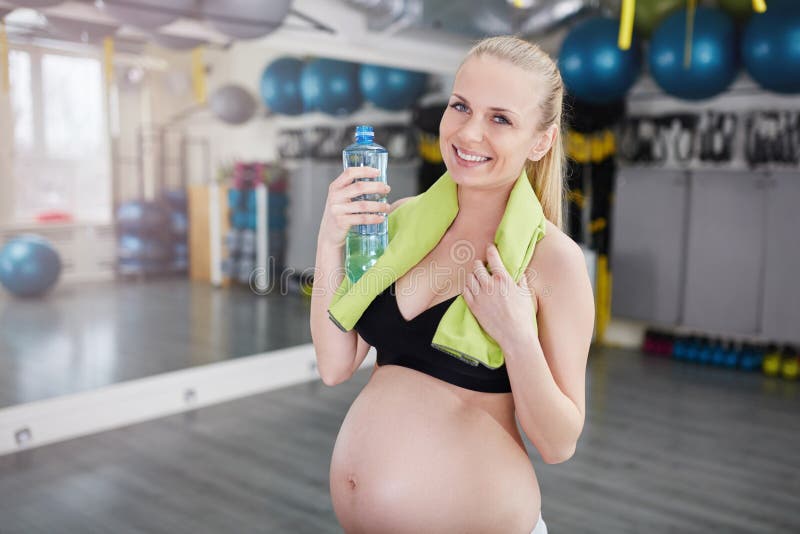 Mooie glimlachende zwangere vrouw bij de fles en de handdoek van de gymnastiekholding stock afbeeldingen Mooie glimlachende zwangere vrouw bij de fles en de handdoek van de gymnastiekholding stock afbeeldingen