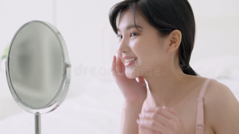 Mooie jonge aziatische vrouw die glimlacht kijkt naar een spiegel van het controleren van gezicht met huidverzorging en cosmetisch