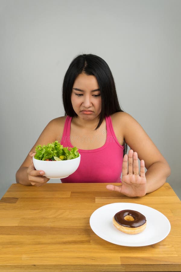 Mooie jonge Aziatische vrouw die saladekom kiezen en chocoladedoughnut verwerpen royalty-vrije stock afbeelding Mooie jonge Aziatische vrouw die saladekom kiezen en chocoladedoughnut verwerpen royalty-vrije stock afbeelding