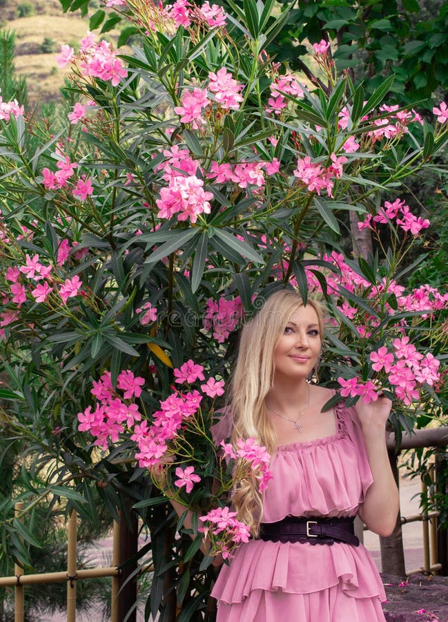 Mooie jonge blonde vrouw in een roze jurk staat buiten in de buurt van een struik met bloemen royalty-vrije stock foto's Mooie jonge blonde vrouw in een roze jurk staat buiten in de buurt van een struik met bloemen royalty-vrije stock foto's