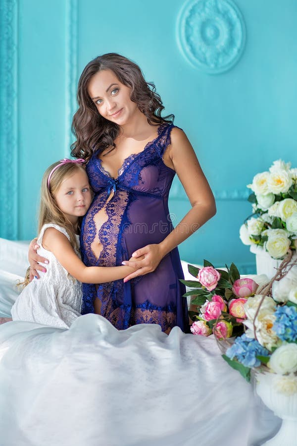 Mooie jonge donkerbruine zwangere vrouw in ontzagwekkende sexy purpere kleding dicht bij blauwe bank en leuke bloemen samen met d stock foto Mooie jonge donkerbruine zwangere vrouw in ontzagwekkende sexy purpere kleding dicht bij blauwe bank en leuke bloemen samen met d stock foto
