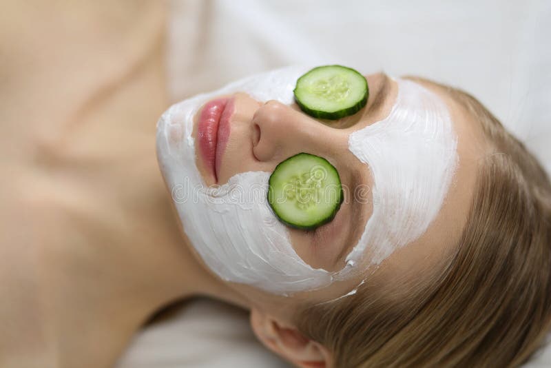 Mooie jonge vrouw die gezichtsmasker van komkommer in schoonheidssalon ontvangen stock foto Mooie jonge vrouw die gezichtsmasker van komkommer in schoonheidssalon ontvangen stock foto