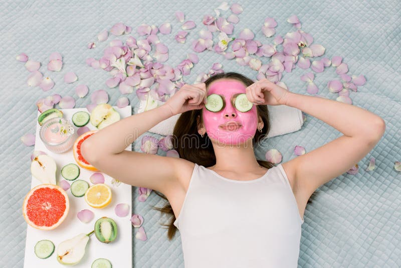 Beautiful young woman with facial mask on her face holding slices of fresh cucumber. Skin care and treatment, spa, natural beauty and cosmetology concept. Beautiful young woman with facial mask on her face holding slices of fresh cucumber. Skin care and treatment, spa, natural beauty and cosmetology concept.