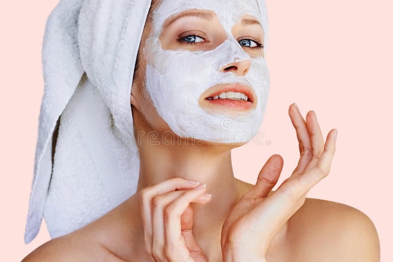 Beautiful young woman with facial mask on her face. Skin care and treatment, spa, natural beauty and cosmetology concept, over pink background. Beautiful young woman with facial mask on her face. Skin care and treatment, spa, natural beauty and cosmetology concept, over pink background