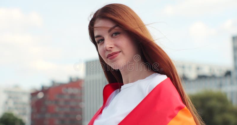 Beautiful young woman with long red hair covering in a rainbow flag Alone. One. Keeping fist up, covering LGBT flag. Beautiful young woman with long red hair covering in a rainbow flag Alone. One. Keeping fist up, covering LGBT flag