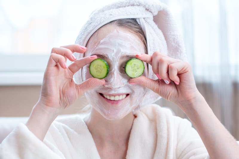 Beautiful happy young woman with natural cosmetic mask and cucumber slices on her face. Concept skin care and Spa treatments at home. Beautiful happy young woman with natural cosmetic mask and cucumber slices on her face. Concept skin care and Spa treatments at home
