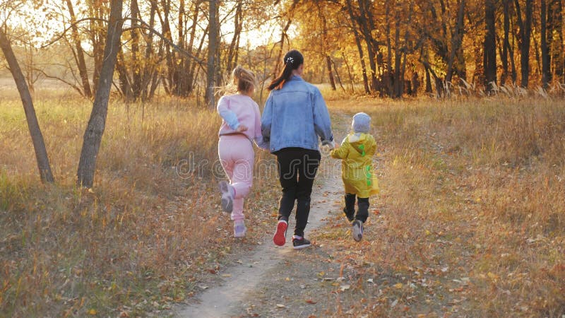 Mooie jonge vrouw met twee kinderen die in het herfstbos lopen. gelukkig gezin dat samenkomt in de natuur waar ze van houden