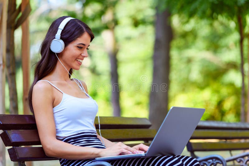 Mooie jonge vrouwenzitting op bank in het park, die laptop computer met behulp van royalty-vrije stock afbeelding Mooie jonge vrouwenzitting op bank in het park, die laptop computer met behulp van royalty-vrije stock afbeelding