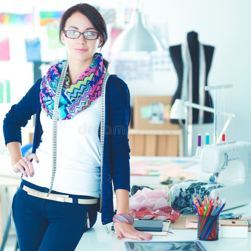 Mooie manierontwerper die zich dichtbij bureau in studio bevinden stock afbeeldingen Mooie manierontwerper die zich dichtbij bureau in studio bevinden stock afbeeldingen