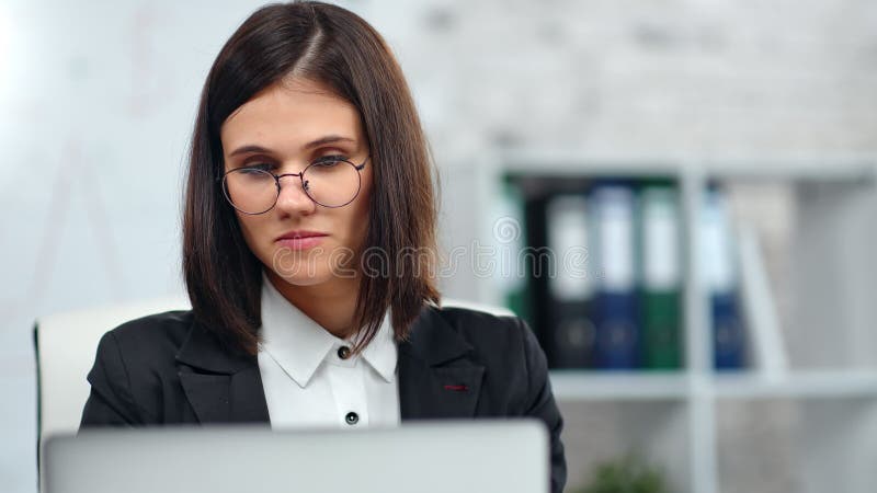 Mooie, penibele boekhouder van een vrouwelijke kantoorarbeider die het computerscherm op de witte werkplek bekijkt