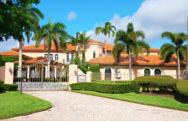 Beautiful Spanish style luxury mansion residential home with a privacy gate and palm trees on a blue sky sunny morning. Beautiful Spanish style luxury mansion residential home with a privacy gate and palm trees on a blue sky sunny morning.